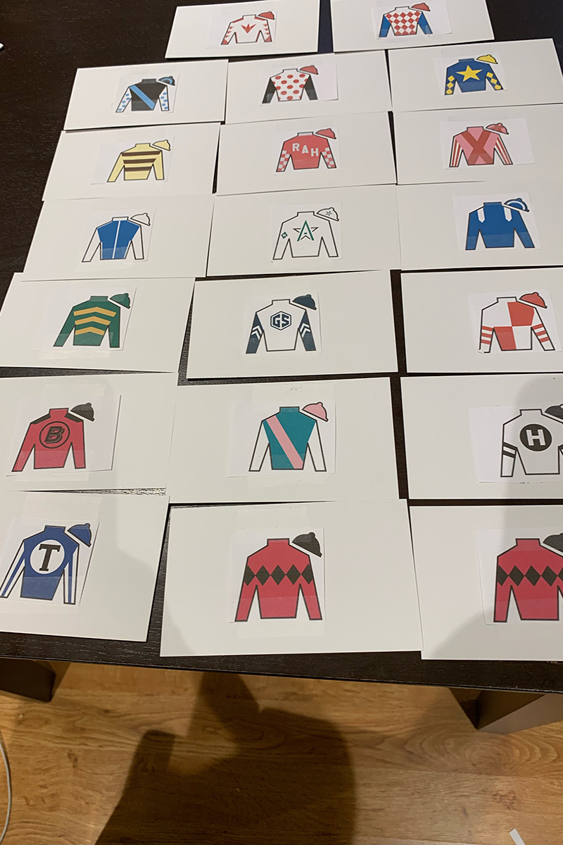 Photo of the pristine white notecards, each with individual colorful cartoon-like outlines of Jockey silks/shirts that Larry Colmus makes prepare for announcing the Kentucky Derby. The notecards are lined up in rows on a table.