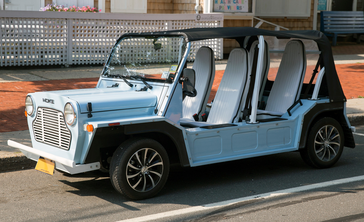 Photo of a light blue Moke car with the doors are and a black soft top on.