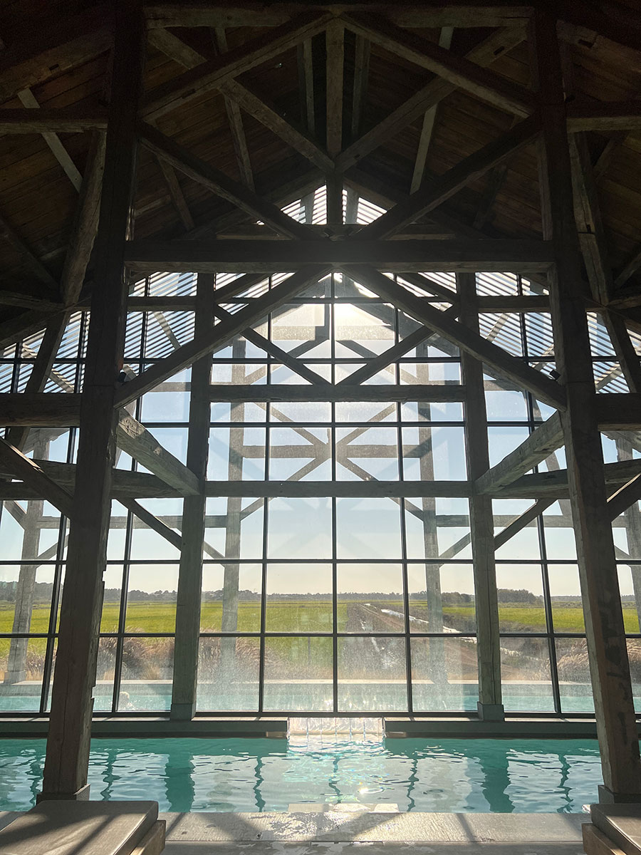 Photo taken straight on from the inside of the Sublime Comporta Beach Club looking out the large floor-to-ceiling-windows with the heated pool just below them. 