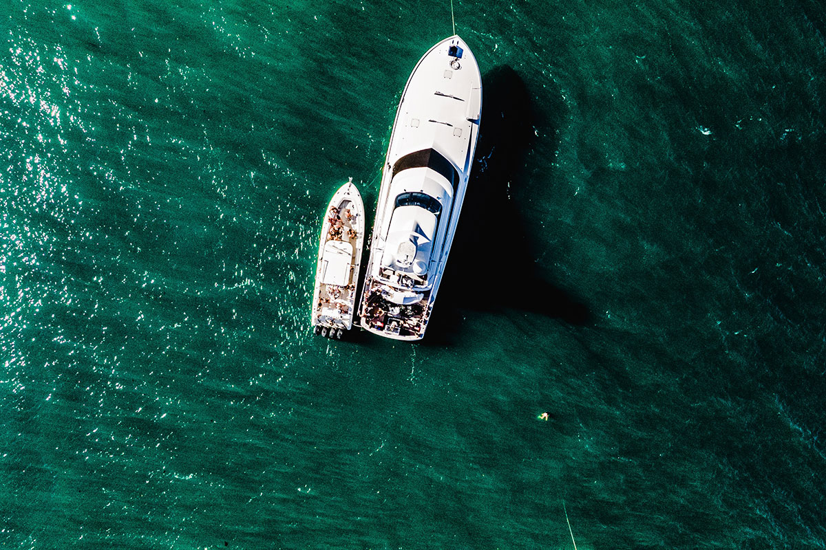 Aerial photo take of two white charter boats in Montauk in the middle of the dark turquoise water. One is large and the other is smaller and wedged right next to the other.
