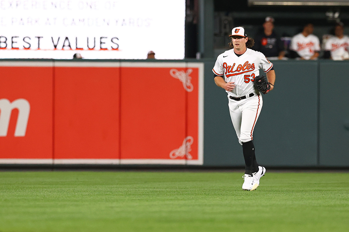 Photo of Baltimore Orioles pitcher Mike Baumann running onto the green baseball field, dressed in the classic white, orange and black Baltimore Orioles uniform.