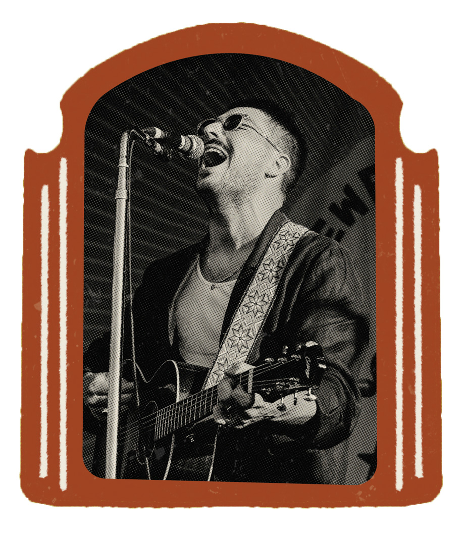 A black and white photo of Marcus Mumford singing in to a microphone on a stand while playing the acoustic guitar strapped around him. There is a poster in the background behind Mumford with angles stripes. Mumford is wearing sunglasses and has on a dark jacket with a white under shirt. The photo itself is framed by an illustrated frame in a burgundy color.