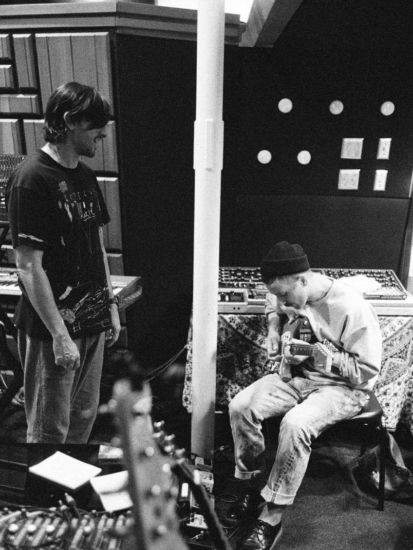 Portugal. The Man in the studio playing guitar in a black and white photo. 