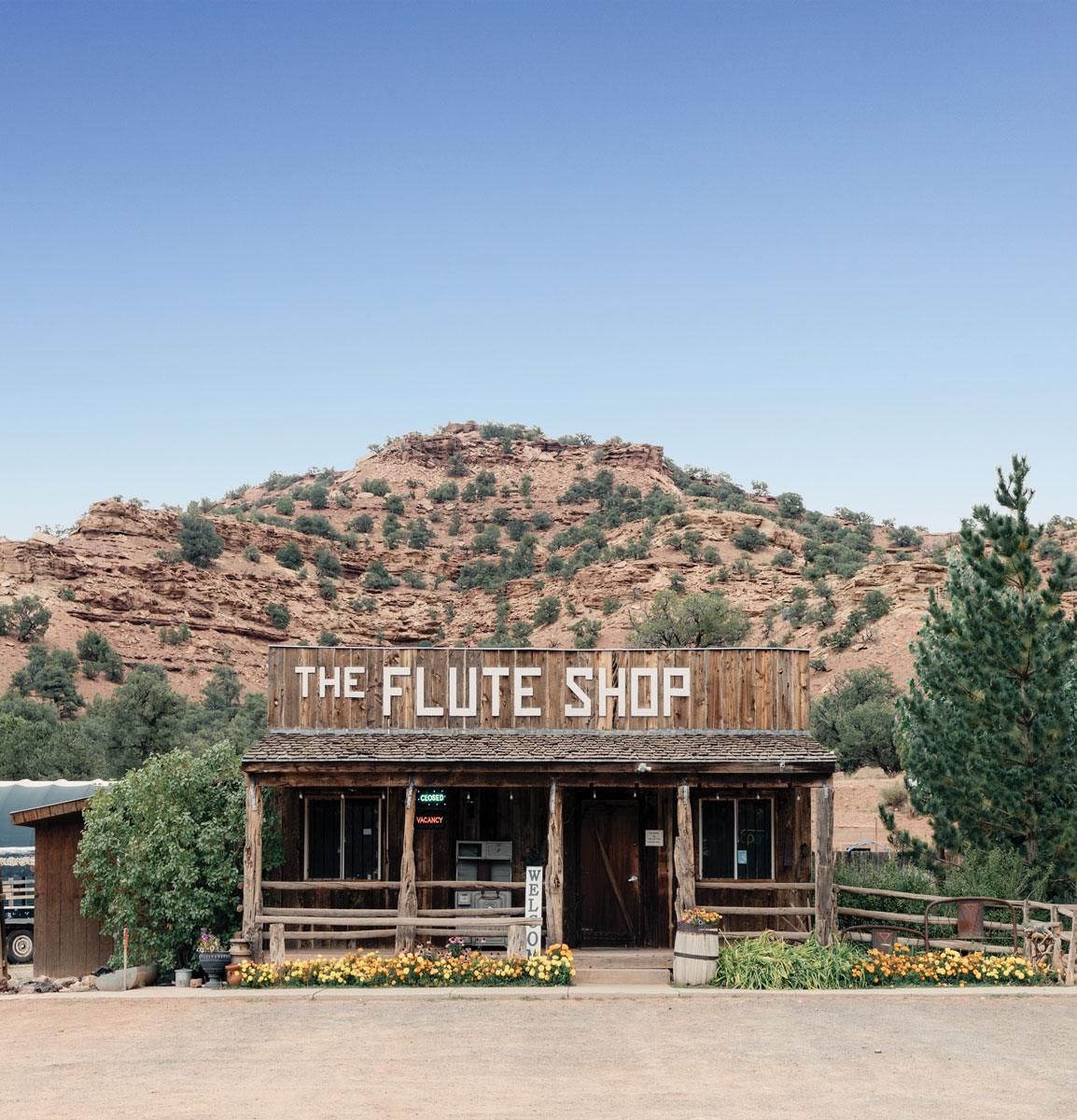Front of the wooden storefront with big letters that spell "The Flute Shop" in front of a desert mountain landscape.