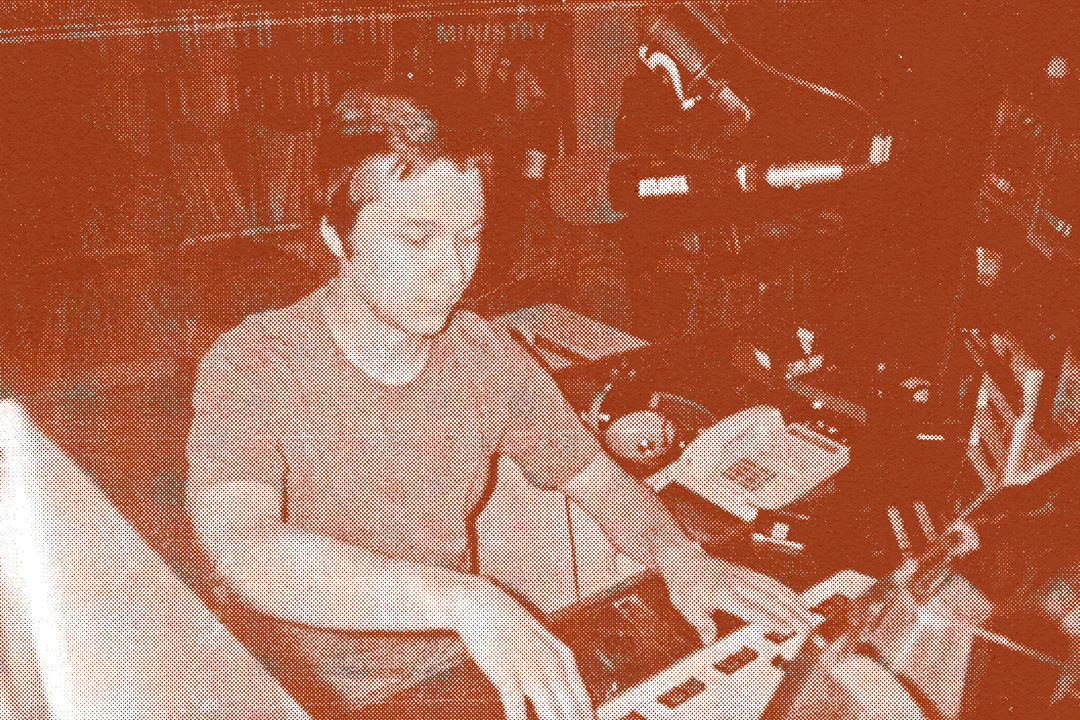 Young man in a DJ booth adjusting levels on a sound board in front of him. There is a large microphone hanging from above that is pointed towards his face and the desk aread is stacked with sound equipment. Behind the man are shelves and shelves of stacked records. The image has a dark red-colored overlay and a halftone texture on them.