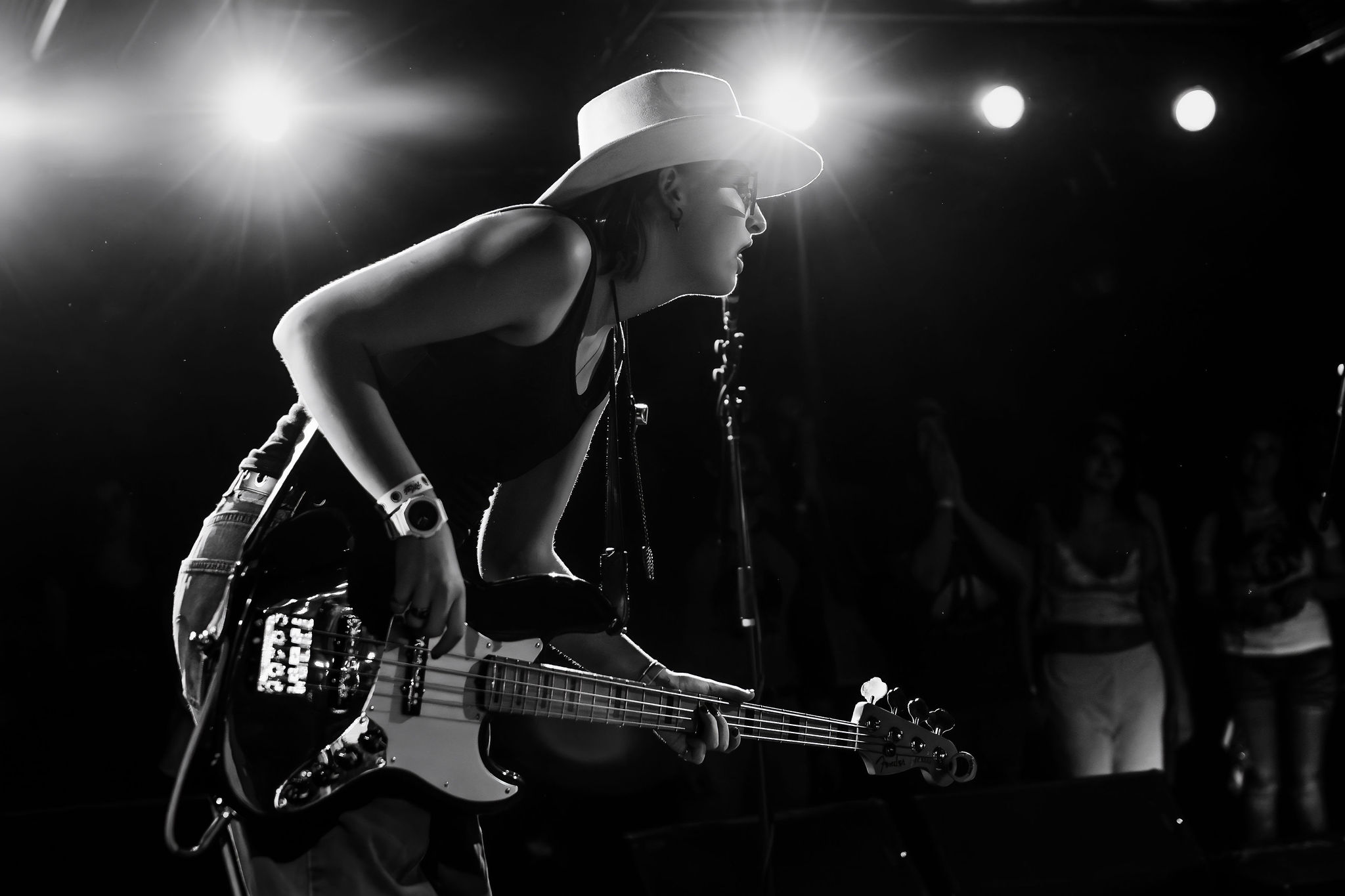 A bassist with a hat on playing while leaning into the crowd