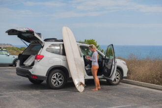 A woman standing in front of a car with a surfboard