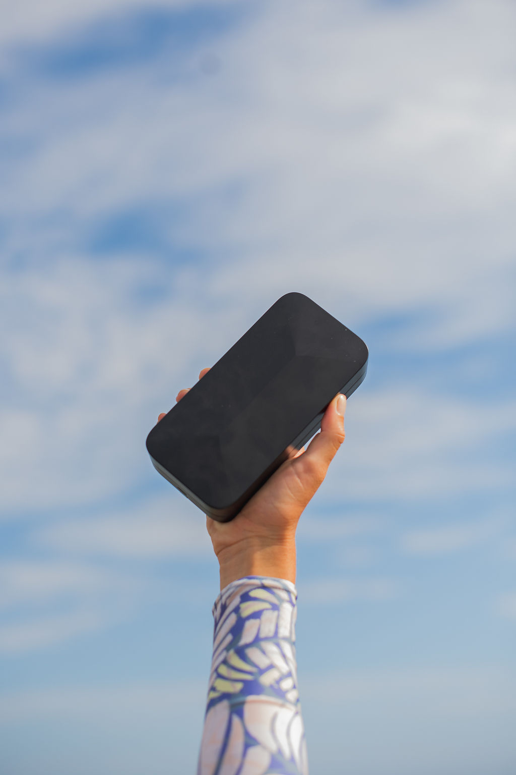A hand holding up a TROVA safe in front of a blue sky