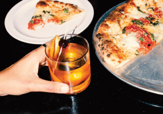 Bulleit Bourbon and a pizza pie in the background with a half eaten slice waiting on a white plate.
