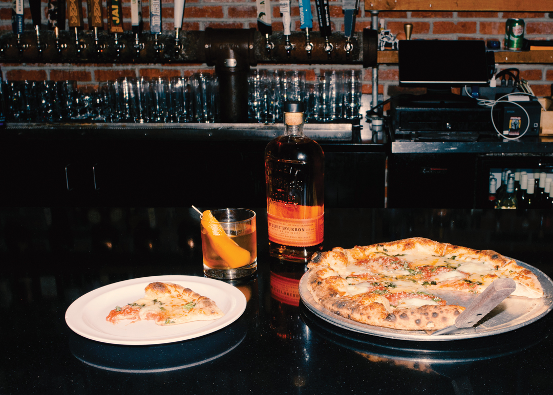 Bottle of Bulleit with a pizza pie placed in front of a bar.