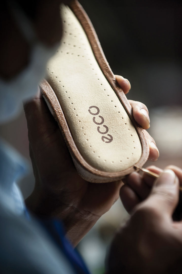 A close up shot of cobbler's hands as they hold the bottom part of a shoe and uses a tool to work on the shoo.