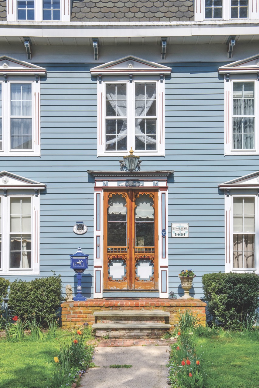 Front of a Victorian style blue house with white windows. 