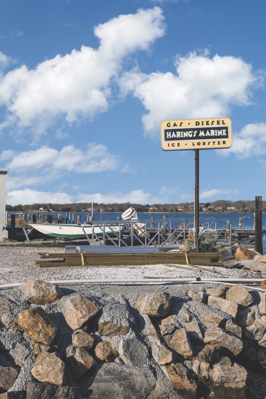 boat dock with rocks in the foreground and a sign in the background advertising haring's marine: gas, diesel, ice, lobster. 