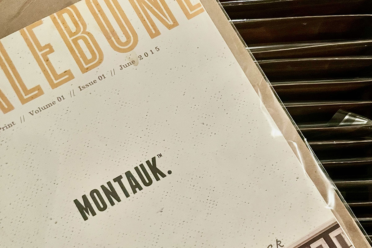 Close-up photo of the Montauk Issue of Whalebone Magazine. The magazine is resting diagonally on top of the file drawer containing the rest of Matthew's collection. The cover is white with gray specks and the word "MONTAUK." is in black and in the center. At the top of the magazine, the classic Whalebone blockstyle header is in yellow with the details including the volume number, issue number and date of publication in smaller black typecase below. 